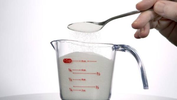 a hand pouring sugar into a measuring cup